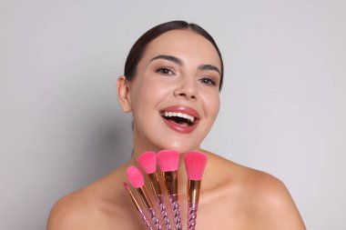 Açık gri arka planda makyaj fırçası olan güzel bir kadın.