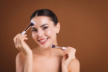 Kahverengi arkaplanda makyaj fırçası olan güzel bir kadın, metin için boşluk