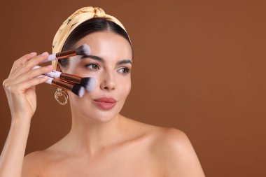 Kahverengi arkaplanda makyaj fırçası olan güzel bir kadın, metin için boşluk