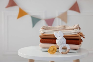 İçerideki beyaz masada temiz bebek kıyafetleri ve aksesuarlar yığını.