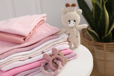 İçerideki beyaz masada temiz bebek kıyafetleri ve oyuncaklar yığını, yakın plan.