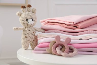 İçerideki beyaz masada temiz bebek kıyafetleri ve oyuncaklar yığını, yakın plan.