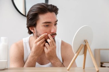 Akne sorunu olan genç bir adam içerideki masaya aynaya bakıyor.