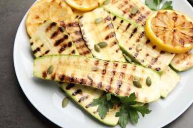 Lezzetli ızgara kabak dilimleri, balkabağı tohumları, limon ve maydanoz, gri masanın üstünde, üst tarafta.