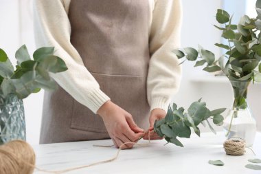 Çiçekçinin beyaz mermer masasında okaliptüs dallarından güzel bir buket yapıyor.