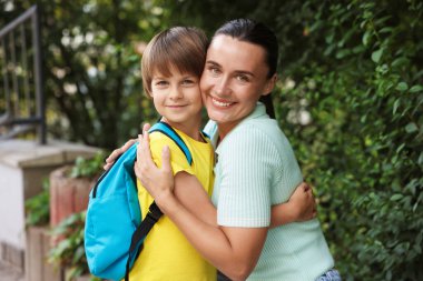 Anne, oğlunu okula götürürken ona sarılıyor.