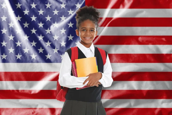 ABD bayrağına karşı sırt çantası ve defterleri olan küçük bir kız. Dil okulu