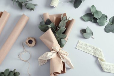 Çiçekçi. Beyaz masa üzerinde okaliptüs dalları, iplikler, kurdele ve ambalaj kağıdı düz.