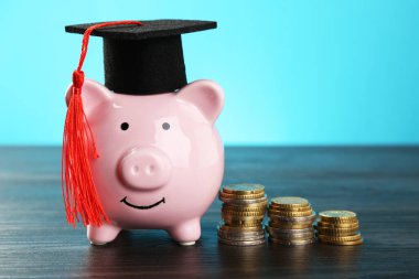 Burs. Mezuniyet şapkası, domuz kumbarası ve paralar açık mavi arka planda, yakın plan.