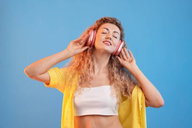 Mutlu kadın kulaklıkla müzik dinliyor ve açık mavi arka planda dans ediyor.