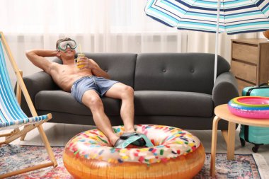 Dalgıç maskeli ve yüzgeçli mutlu bir adam. Evdeki kanepede bir kavanoz meyve suyu ve şişme yüzük taşıyor. Denizde tatilin hayalini kuruyorum.