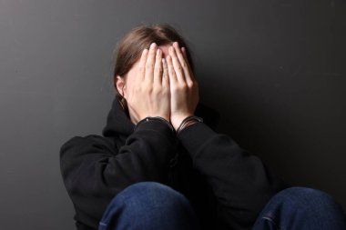 Metal kelepçeli bir kadın ve gri duvarın yanında elleri olan kapüşonlu bir kadın.