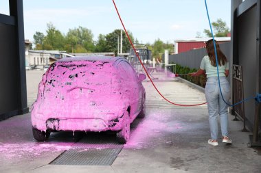 Kadın oto yıkamada köpükle araba yıkıyor.