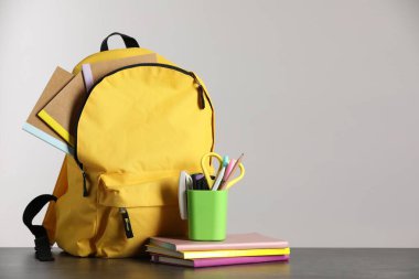 Masanın üzerinde farklı kırtasiye malzemesi olan sarı sırt çantası. Metin için boşluk