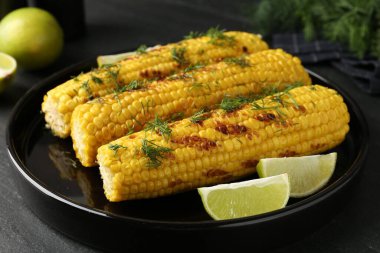 Lezzetli ızgara mısır koçanlarıyla siyah masada dereotu ve limon dilimleri, yakın plan.