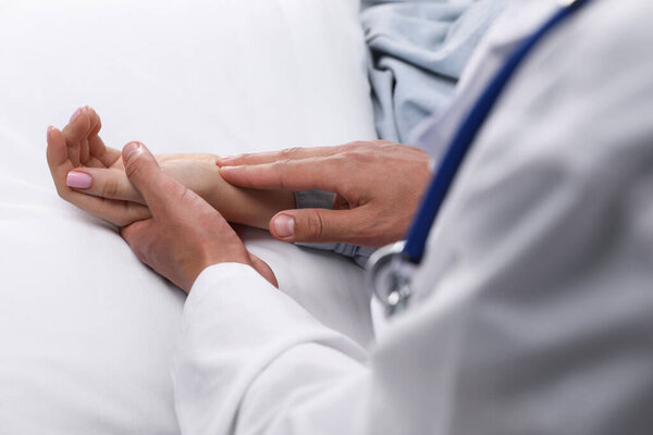 Врач проверяет пульс женщины пальцами дома, крупным планом