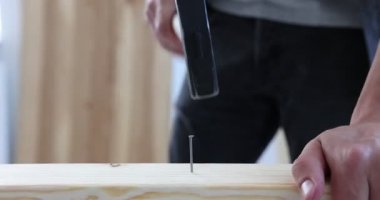 Kapalı alanda tahta çiviye çivi çakan bir adam var.