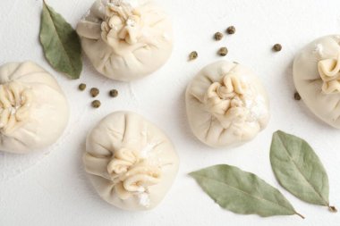 Beyaz masa üzerinde biber ve defne yaprakları ile pişmemiş khinkaliler (hamur tatlısı)