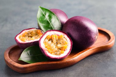 Taze tutku meyveleri ve yeşil yapraklar gri masada, yakın plan.