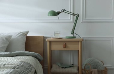 Yatak odasının yanında lamba ve bir bardak su olan komodinin yanında.