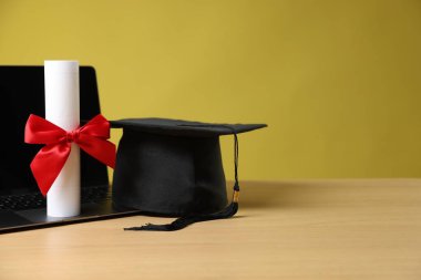 Mezuniyet şapkası, dizüstü bilgisayar ve diploma sarı arka plana karşı ahşap masada. Metin için boşluk