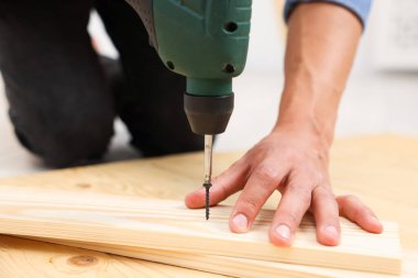 Profesyonel bir tamirci, vidayı içeride elektrikli tornavidayla ahşap tahtaya çeviriyor. Yakın plan.