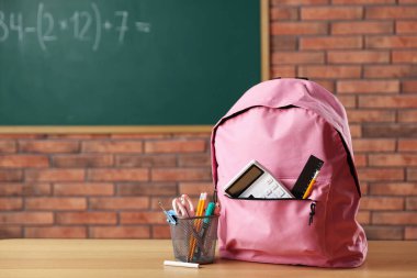 Sınıftaki masasında farklı kırtasiye malzemesi olan pembe bir sırt çantası.