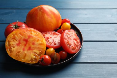 Mavi ahşap masada farklı olgun domatesler, yakın plan.