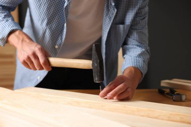 Kapalı alanda tahta çiviye çivi çakan bir adam var.