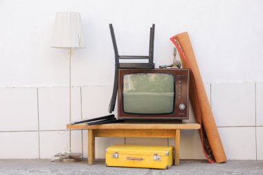 Masa, sandalye, lamba, halı ve valiz beyaz duvarın yanında. Kullanılmış eşyalar