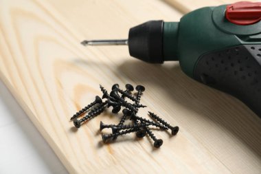 Bir sürü metal vida, elektrikli tornavida ve tahta tahta beyaz masa, yakın plan.