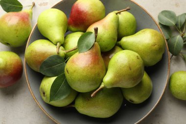 Taze armutlar ve yeşil yapraklar açık gri masada, düz yatıyordu.