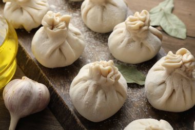 Ahşap masada un, sarımsak ve defne yapraklı pişirilmemiş khinkaliler (hamur tatlısı), yakın plan.