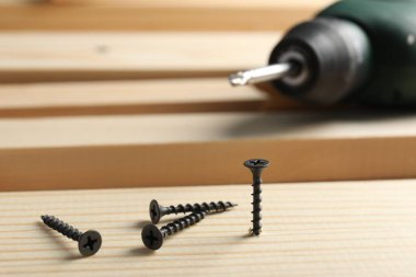 Metal vidalar, elektrikli tornavida ve ahşap döşemeler, yakın plan.