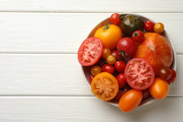 Beyaz ahşap masa üzerinde birçok farklı olgun domates, üst manzara. Metin için boşluk