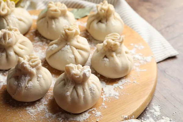 Ahşap masa üzerinde un bulunan pişmemiş khinkaliler (hamur tatlısı), yakın plan.