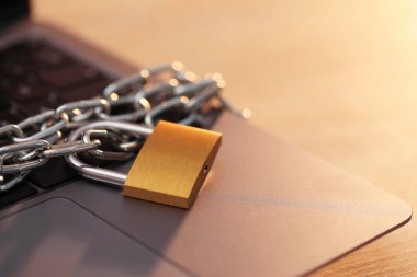 Siber güvenlik. Masada zincir ve dizüstü bilgisayarı olan metal asma kilit, yakın plan.