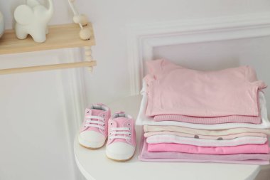 İçerideki beyaz masada temiz bebek kıyafetleri ve ayakkabılar yığını.
