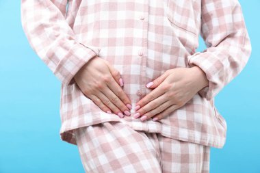 Açık mavi arka planda sistit belirtileri gösteren kadın, yakın plan.