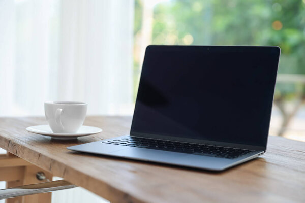 Рабочее место. Ноутбук и чашка напитка на деревянном столе возле окна в помещении, крупный план