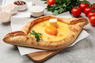 Peynirli, yumurtalı, maydanozlu ve açık gri arkaplanlı diğer ürünlerle lezzetli khachapuri, yakın plan.