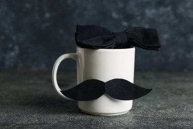 Babalar Günün kutlu olsun. Kâğıt bıyıklı ve papyonlu fincan siyah masanın üstünde, yakın plan.