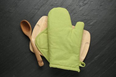 Yeşil fırın eldiveni, ahşap kaşık, tutucu ve masa, üst görüş.