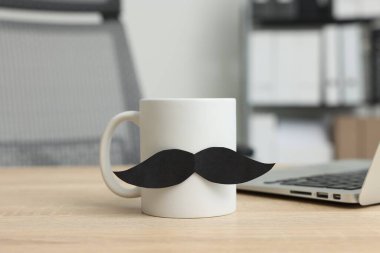 Babalar Günün kutlu olsun. Kağıt bıyıklı ve dizüstü bilgisayarlı bir fincan, ahşap masa, yakın plan.