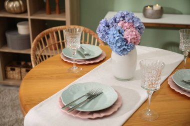 Yemek odasındaki ahşap masada, tabak ve vazo çiçekli şık bir ortam. İç tasarım