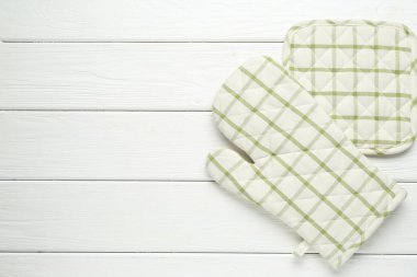 Fırın eldiveni ve tutacağı beyaz ahşap masada, düz yerde. Metin için boşluk