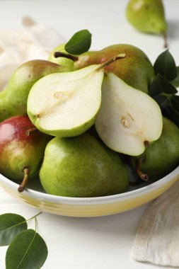 Taze armutlar kasede ve yeşil yapraklar beyaz ahşap masada, yakın plan.