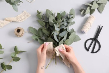 Çiçekçi beyaz masada okaliptüs dallarından güzel bir buket yapıyor.