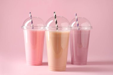 Pembe arka planda plastik bardaklarda lezzetli milkshake.