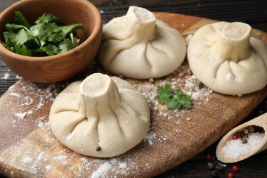 Pişmemiş khinkaliler (hamur tatlısı), baharatlar ve maydanozlar ahşap masada, yakın plan.